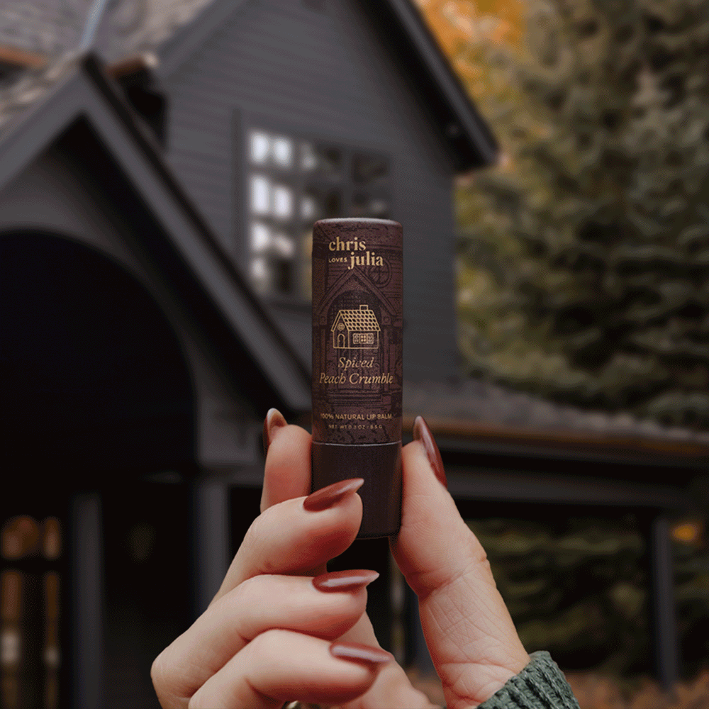 All 3 of the Chris Loves Julia lip balms being held in front of the houses that inspired them.