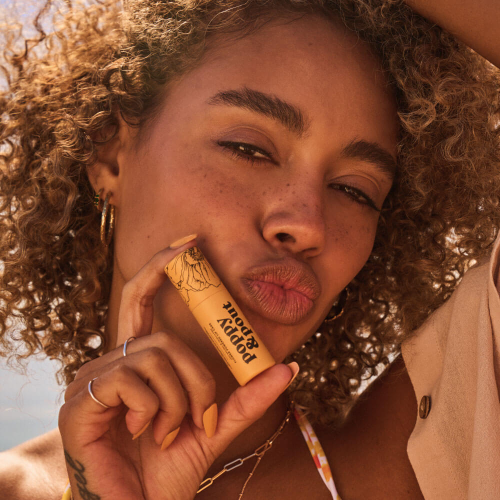 Girl Holding Poppy & Pout Lip Balm by Her Face
