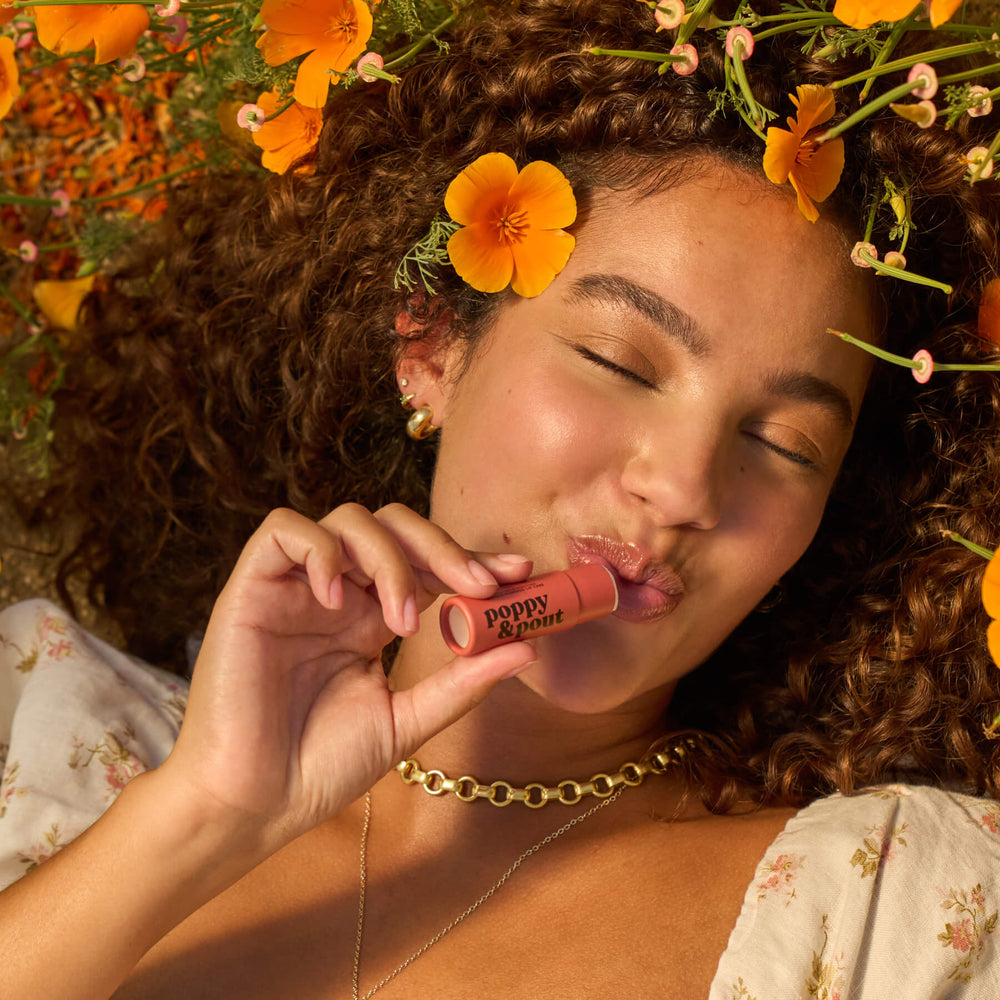 Girl using Poppy & Pout lip balm with flowers in her hair and around her