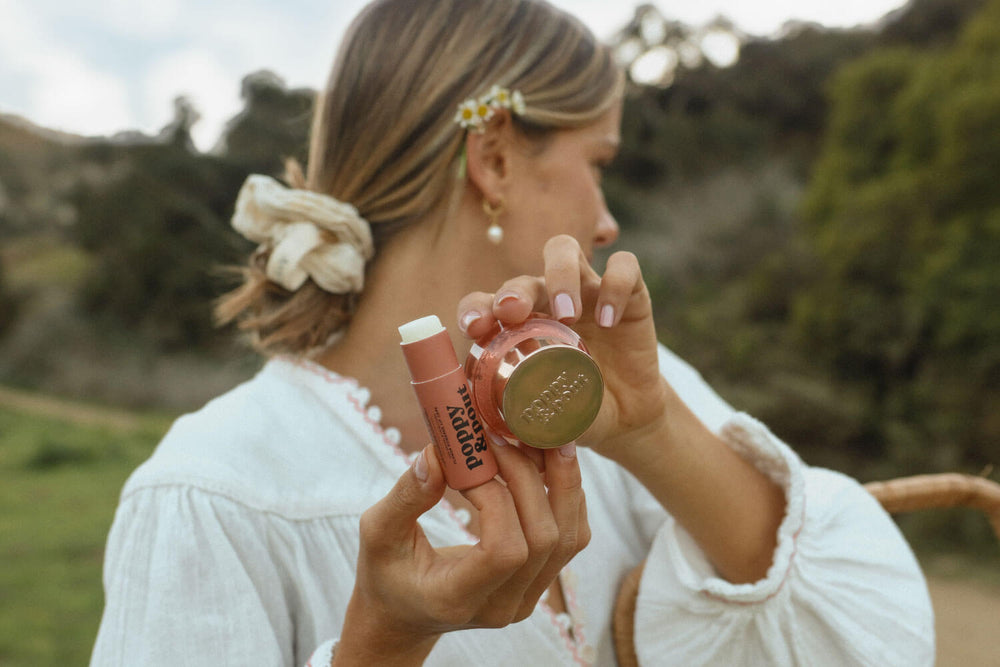 Girl holding a Poppy & Pout lip balm and lip scrub outside. 