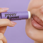 Wild berry lip balm tube, held near glossy lips, purple tube, 3 of 5