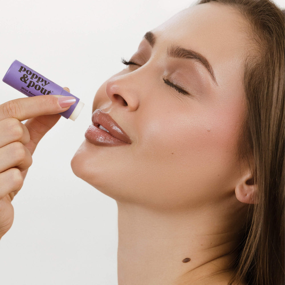 Wild berry lip balm applied to lips, tube held by hand, purple tube